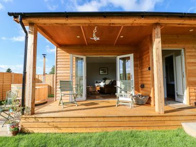 A wooden porch with two chairs and open doors leading to a living room at Rising Sun in Kirkbymoorside