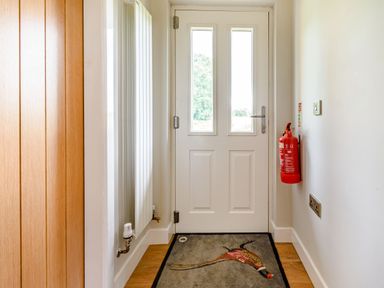 A hallway with a white door a radiator a fire extinguisher and a floor mat with a bird design at Peep o Day in Kirkbymoorside