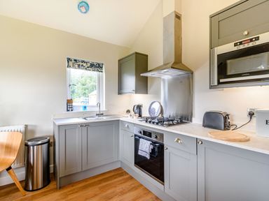 A kitchen with gray cabinets a gas stove oven microwave toaster and a window at Peep o Day in Kirkbymoorside