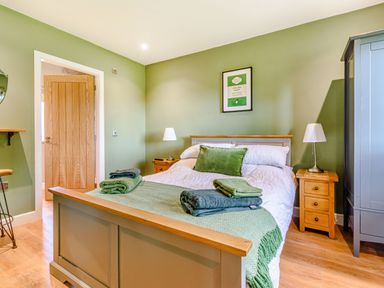 A bedroom with a double bed green walls wooden floor and bedside tables with lamps at Peep o' Day in Kirkbymoorside