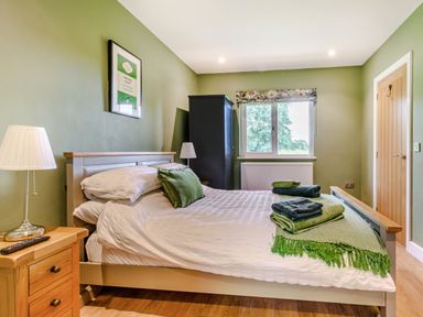 A bedroom with a bed having white bedding and green pillows beside wooden nightstands with lamps and a window with floral valance at Peep o Day in Kirkbymoorside