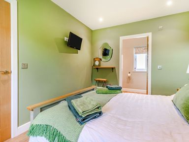 A bedroom with a green wall a bed with folded towels a wall-mounted TV a mirror and a wooden stool at Peep o Day in Kirkbymoorside