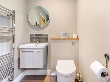 A bathroom with a sink under a round mirror a toilet a towel radiator and a toilet paper holder at Peep o Day in Kirkbymoorside