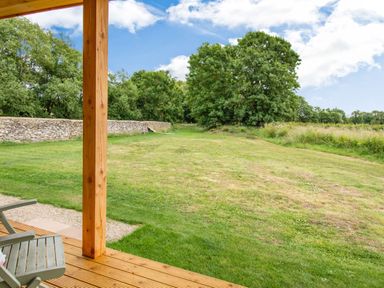 A wooden porch with chairs overlooking a grassy yard with trees and a stone wall at Peep o Day in Kirkbymoorside