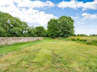 A grassy area with trees and a stone wall under a partly cloudy sky at Peep o Day in Kirkbymoorside
