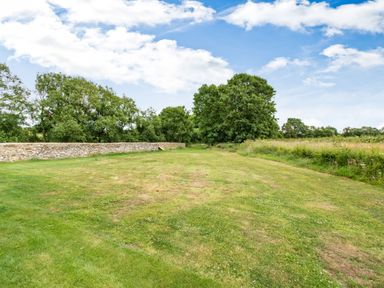A grassy field with trees and a stone wall under a partly cloudy sky at Peep o Day in Kirkbymoorside