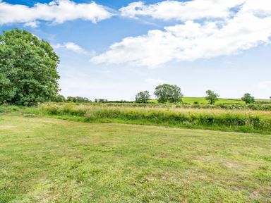 A grassy field with trees under a blue sky at Peep o Day in Kirkbymoorside