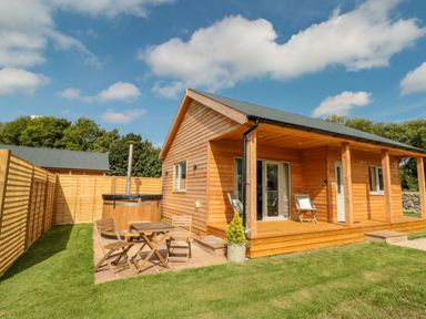 A wooden cabin with a patio table and chairs a hot tub and a porch with chairs at Peep o Day in Kirkbymoorside