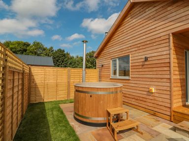 A wooden outdoor hot tub with steps next to a wooden cabin and fenced yard at Peep o Day in Kirkbymoorside