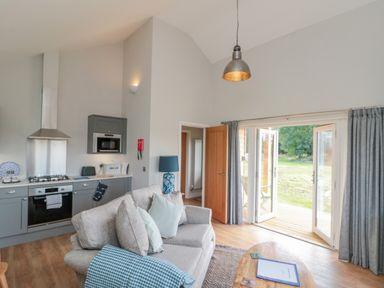 A living room with a gray sofa and kitchen area with gray cabinets and wooden floors at Peep o Day in Kirkbymoorside