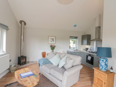 A living room and kitchen area with a gray sofa and wooden coffee table at Peep o Day in Kirkbymoorside