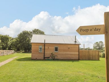 A wooden cabin with a metal roof on a grassy area with a signpost pointing to Peep o day in Kirkbymoorside