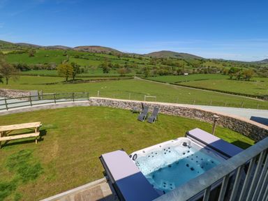 A garden with a hot tub wooden bench and three chairs overlooking green fields and hills at Bwthyn Y Bugail Shepherd's Cottage in Pedairffordd near Llanrhaeadr-Ym-Mochnant
