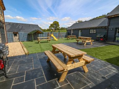 An outdoor courtyard with wooden picnic tables a children's slide and swing set and barbecue grills at Bwthyn Y Bugail Shepherd's Cottage in Pedairffordd near Llanrhaeadr-Ym-Mochnant