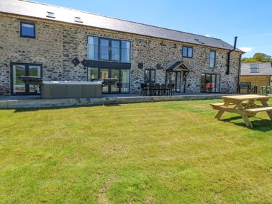 A stone building with a patio table set hot tub and picnic bench on a lawn at Bwthyn Y Bugail Shepherd's Cottage in Pedairffordd near Llanrhaeadr-Ym-Mochnant