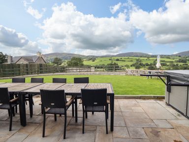 An outdoor patio with a dining table and chairs overlooking a grassy yard and hills at Bwthyn Y Bugail Shepherd's Cottage Pedairffordd near Llanrhaeadr-Ym-Mochnant