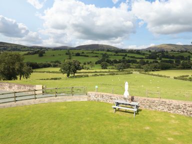 A garden with a picnic table and umbrella overlooking fields and hills at Bwthyn Y Bugail Shepherd's Cottage in Pedairffordd near Llanrhaeadr-Ym-Mochnant