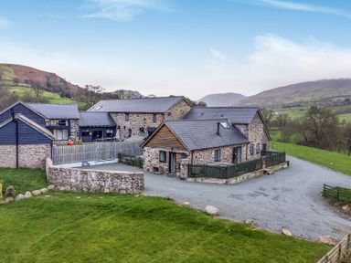 A stone house with a gravel driveway and green lawn at Bwthyn Y Bugail (Shepherd's Cottage) Pedairffordd near Llanrhaeadr-Ym-Mochnant
