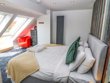 A bedroom with a bed green pillows a red armchair and large windows at Y Granar Llanrhaeadr-Ym-Mochnant