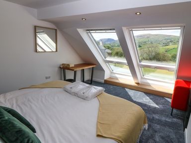 A bedroom with a bed near two large windows showing a hillside at Y Granar The Granary in Llanrhaeadr-Ym-Mochnant