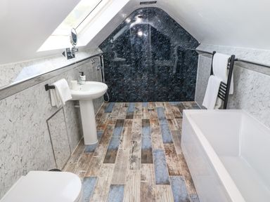 A bathroom with a bathtub toilet and sink under a sloped ceiling at Y Granar Llanrhaeadr-Ym-Mochnant