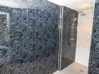 A shower area with dark marbled walls and a handheld and overhead shower at Y Granar Llanrhaeadr-Ym-Mochnant