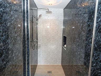A walk-in shower with black and white marble walls and a tiled floor at Y Granar The Granary Llanrhaeadr-Ym-Mochnant