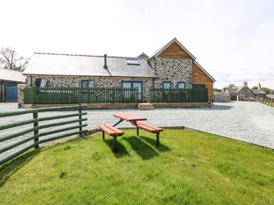 A stone and wood house with green fencing gravel driveway and a red picnic table on grass at Y Granar The Granary in Llanrhaeadr-Ym-Mochnant