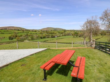 A red picnic table on grass with a fenced green hillside landscape and blue sky at Y Granar in Llanrhaeadr-Ym-Mochnant