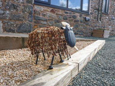 A metal sheep sculpture on gravel outside a stone building at Y Granar The Granary in Llanrhaeadr-Ym-Mochnant