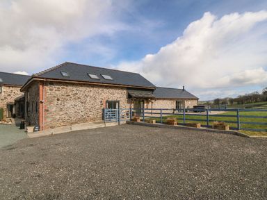 An exterior view of a stone house with a gravel driveway and a fenced lawn at Y Granar The Granary in Llanrhaeadr-Ym-Mochnant