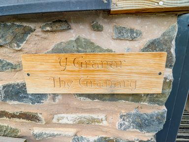 A wooden sign with the text Y Granar The Granary on a stone wall at Y Granar (The Granary) in Llanrhaeadr-Ym-Mochnant