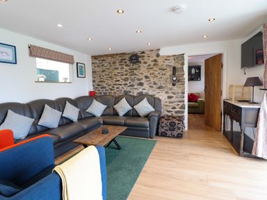 A living room with a leather sectional sofa cushions a wooden coffee table and a stone accent wall at Y Granar in Llanrhaeadr-Ym-Mochnant