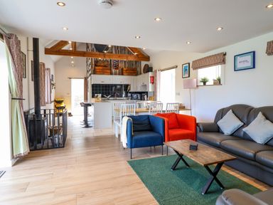 An open plan living room and kitchen with blue and red armchairs a grey sofa a wooden coffee table and a dining table with white chairs at Y Granar Llanrhaeadr-Ym-Mochnant