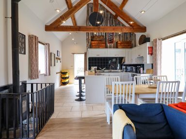 A kitchen and dining area with wooden beams white cabinets a dining table with chairs and a blue sofa at Y Granar Llanrhaeadr Ym Mochnant