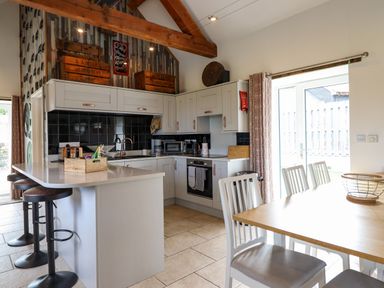 A kitchen with white cabinets a central island with stools and a dining table with chairs at Y Granar The Granary in Llanrhaeadr-Ym-Mochnant