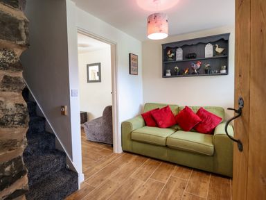 A small living area with a green sofa with red cushions a wall shelf with decorative items and a carpeted staircase at Y Granar The Granary in Llanrhaeadr-Ym-Mochnant