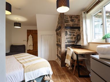 A bedroom with a bed a wooden desk and chair stone wall and window at Y Granar The Granary in Llanrhaeadr-Ym-Mochnant