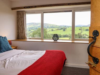 A bedroom with a bed and large window showing green hills at Y Granar The Granary in Llanrhaeadr-Ym-Mochnant