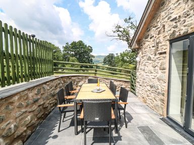 An outdoor patio with a rectangular table and six chairs next to a stone wall at Y Stabl in Llanrhaeadr-Ym-Mochnant