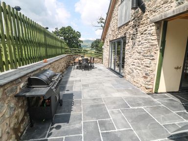 An outdoor patio with a barbecue grill and dining table next to a stone house at Y Stabl Llanrhaeadr-Ym-Mochnant