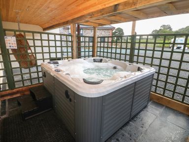An outdoor covered area with a bubbling hot tub next to a green lattice fence at Y Stabl The Stable in Llanrhaeadr-Ym-Mochnant