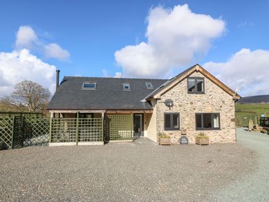 A stone house with a slate roof skylights and green lattice fencing in a rural setting at Y Stabl The Stable in Llanrhaeadr-Ym-Mochnant