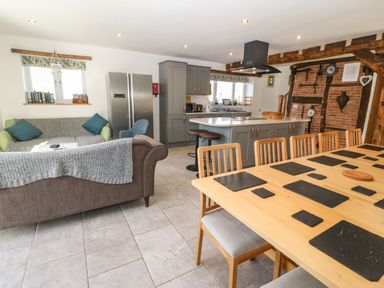 A kitchen and dining area with wooden dining table and chairs gray cabinets sofas and a large refrigerator at Y Stabl (The Stable) in Llanrhaeadr-Ym-Mochnant
