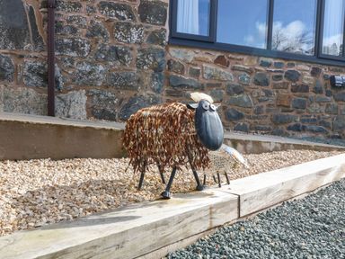 A metal sheep sculpture on gravel outside a stone building at Y Stabl The Stable in Llanrhaeadr Ym Mochnant
