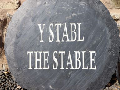 A black stone sign with the text Y Stabl The Stable on a stone wall background at Y Stabl The Stable in Llanrhaeadr-Ym-Mochnant