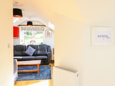 A living room with a black sofa a wooden coffee table and two black ceiling lamps at Y Stabl (The Stable) in Llanrhaeadr-Ym-Mochnant