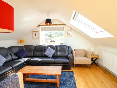 An attic living room with a black leather sectional sofa beige armchair wooden coffee table and skylight window at Y Stabl The Stable in Llanrhaeadr Ym Mochnant