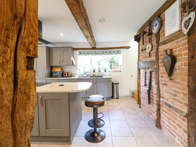 A kitchen with grey cabinets a kitchen island with stools a window and a brick wall with decorations at Y Stabl The Stable in Llanrhaeadr-Ym-Mochnant
