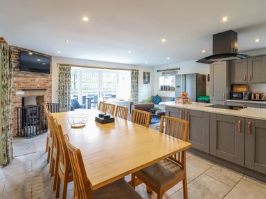 A kitchen and dining area with a wooden table and chairs a brick fireplace and gray cabinets at Y Stabl in Llanrhaeadr-Ym-Mochnant